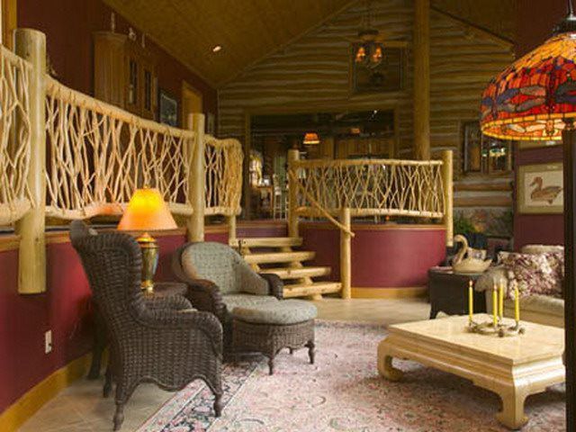 Cozy log cabin interior with twig railing, armchairs, and a low table on a patterned rug.