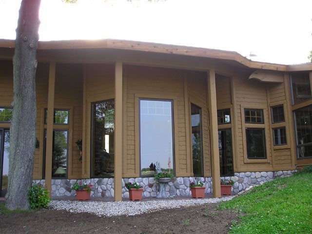 Brown house with stone base, large windows, and porch supported by wooden columns.