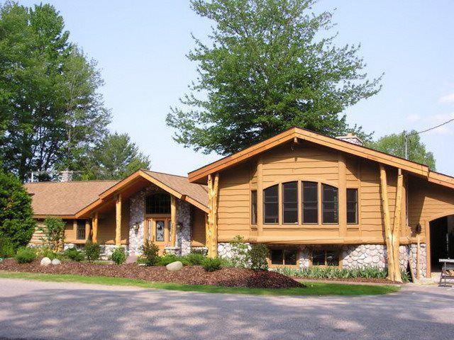 Brown wooden house with stone accents, brown roof, and arched windows, surrounded by trees.
