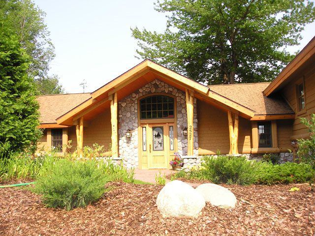 Rustic home with stone and wood facade, arched window, and landscaped yard.