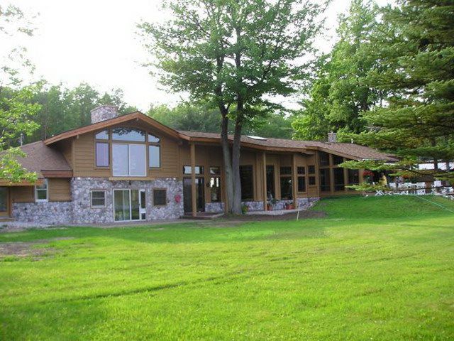 Large, wood-sided house with stone accents, on a grassy lawn, surrounded by trees.