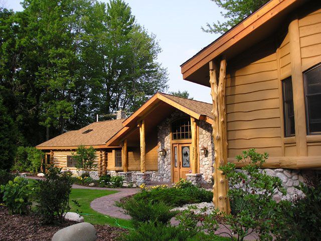 Rustic log cabin-style house with stone and wooden accents, front entrance, path, and surrounding greenery.