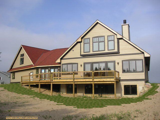 Tan house with red roof, wooden deck, large windows, and chimney against a blue sky.