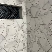 A close up of a shower with hexagon tiles and a shelf.