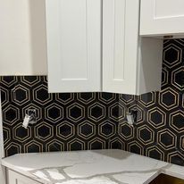 A kitchen with black and gold tiles and white cabinets.