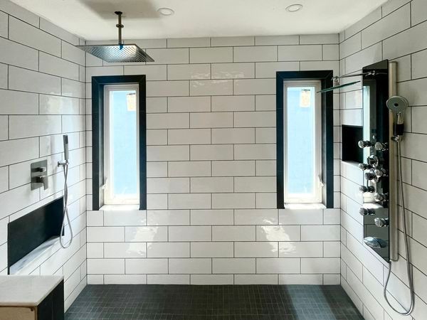 A bathroom with white tiles and two windows.
