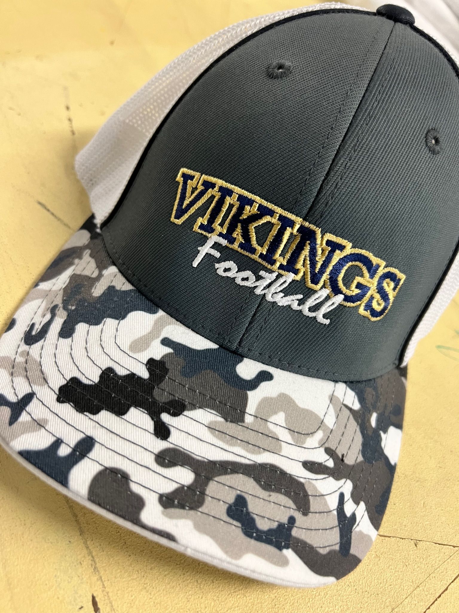 Custom embroidery featuring Navy and camo Vikings football cap with gold lettering and white mesh.