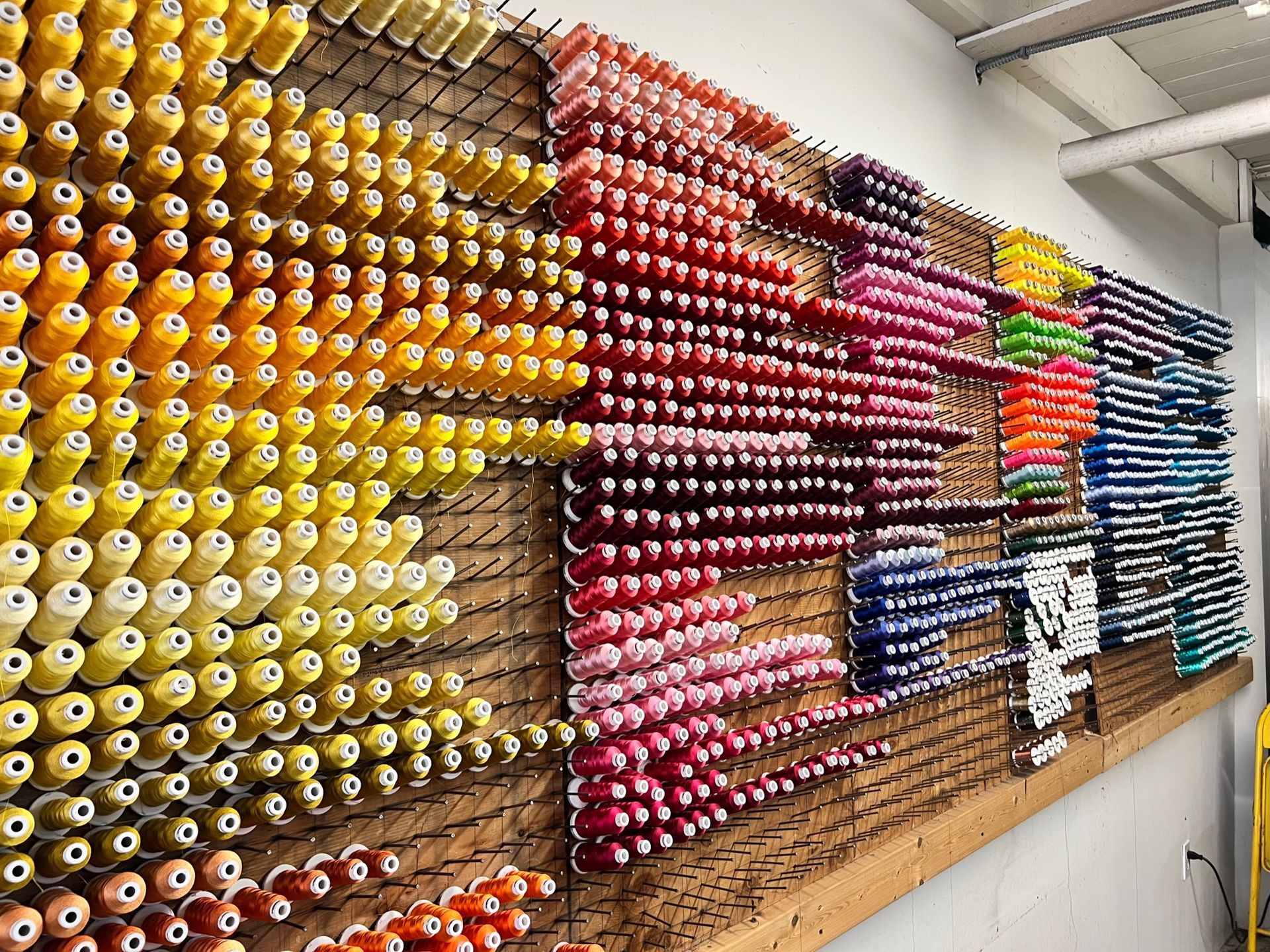 Colorful spools of custom embroidery thread arranged on a wooden board. Shades of yellow, red, pink, and blue.