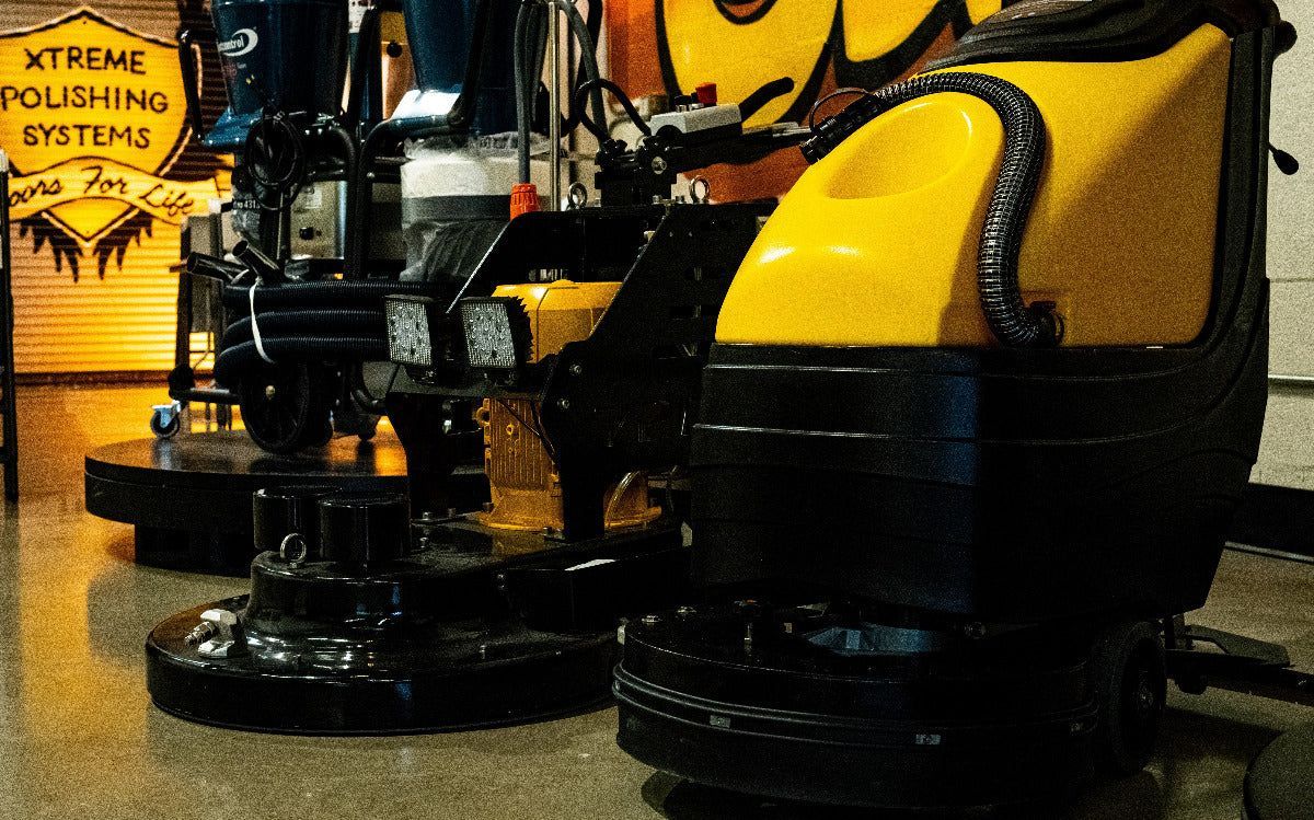 A person operates a yellow floor cleaning machine on a wet, gray floor.