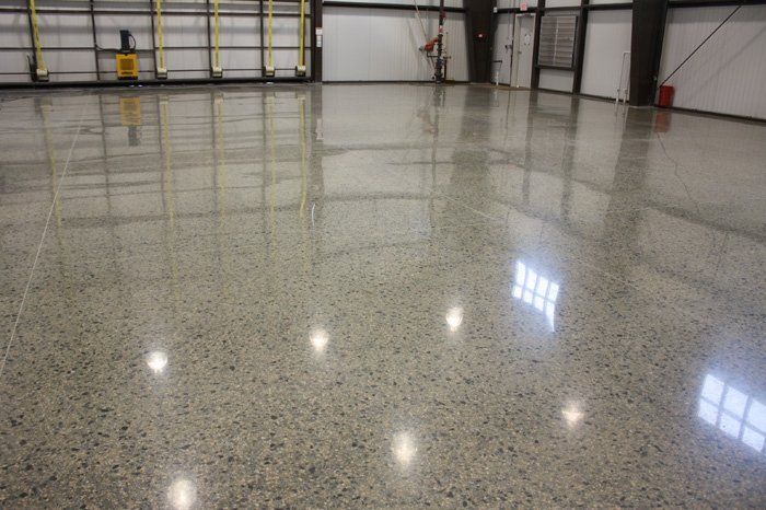 Polished concrete floor reflecting an empty industrial space with overhead lighting.