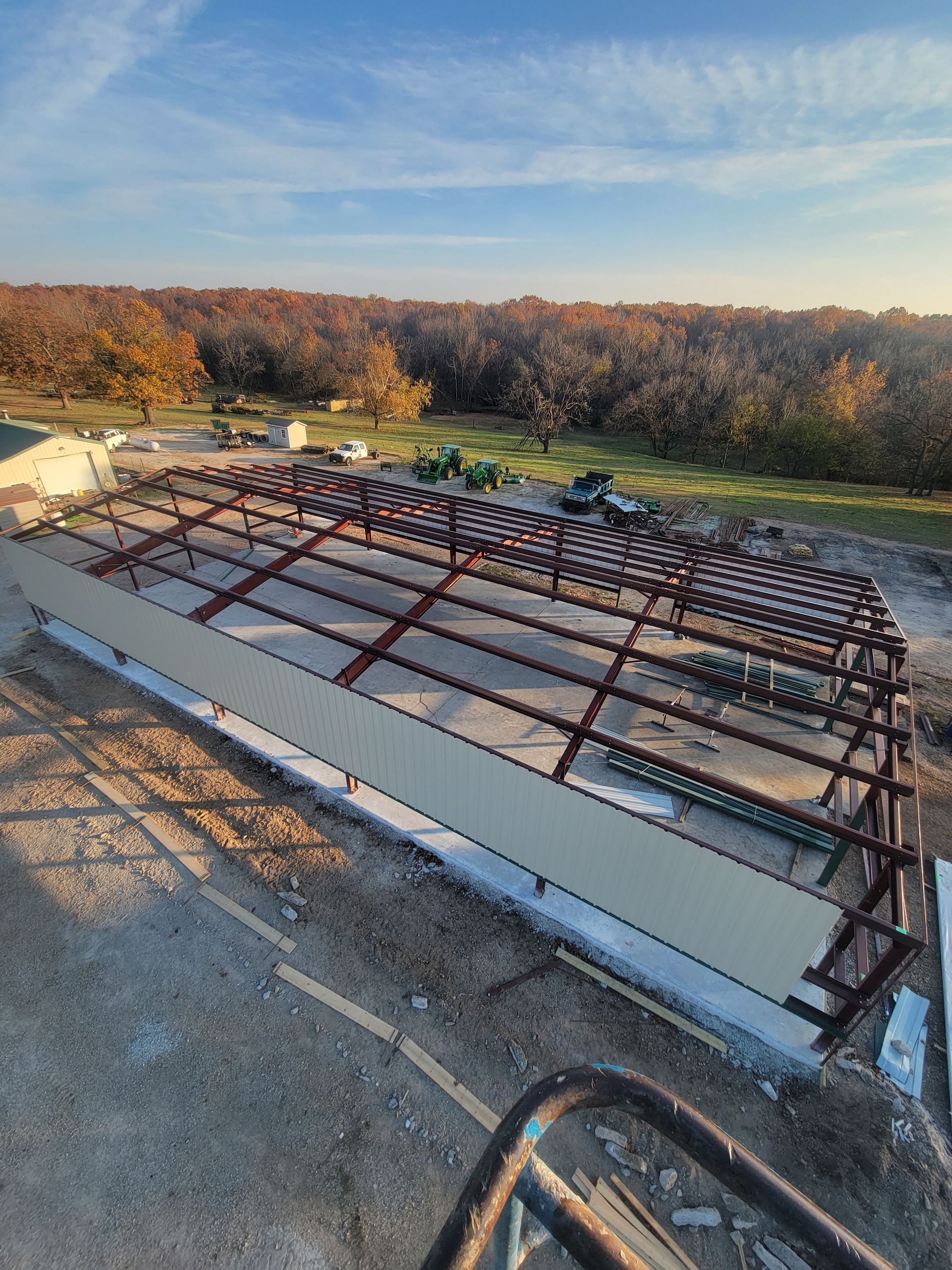 Steel framework of a building under construction, with attached wall panels. Trees and sky in the background.