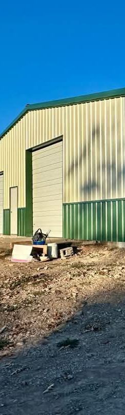 Metal building with a green roof and trim, blue sky, and a person sitting on a platform outside.