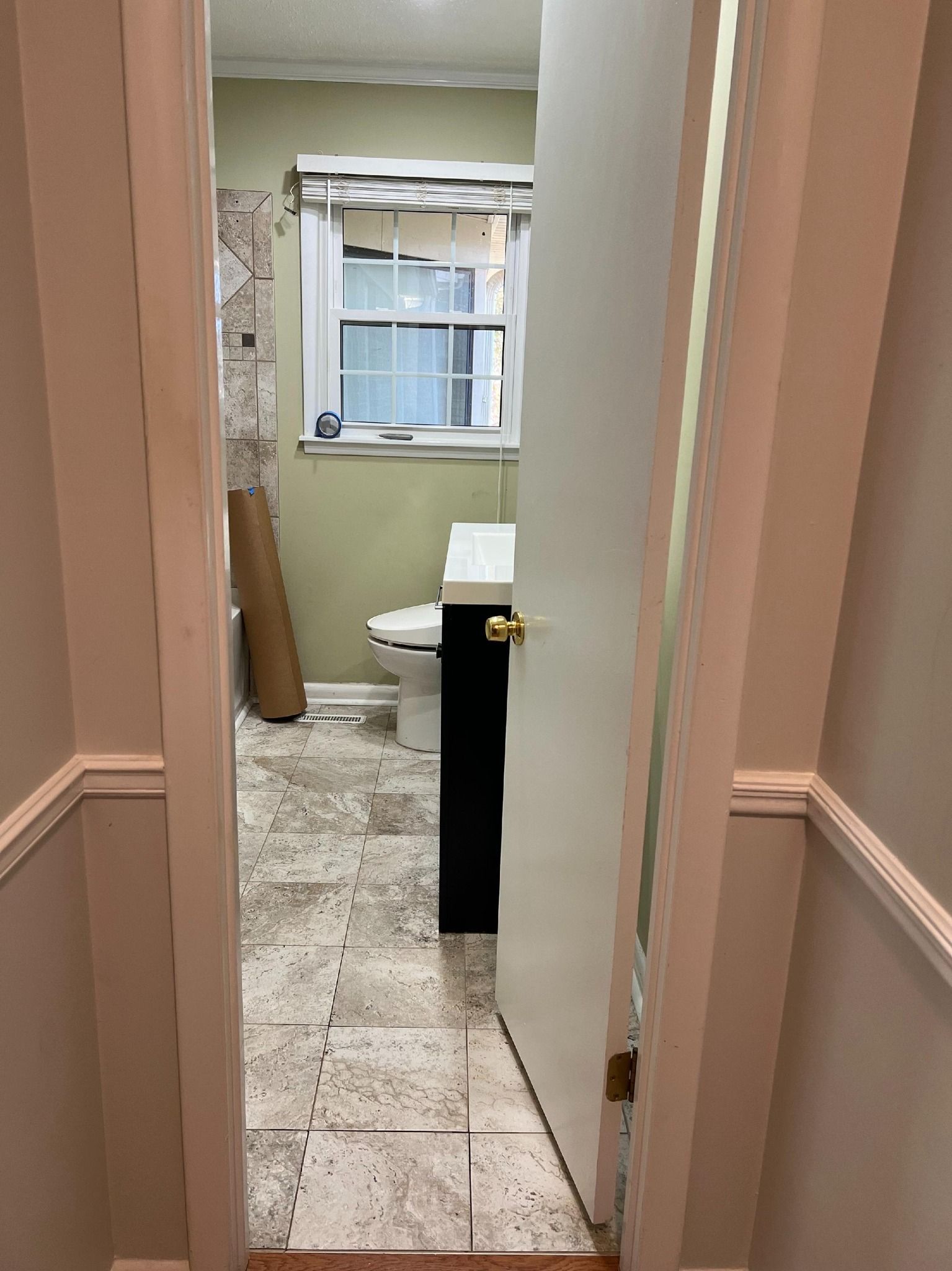 Bathroom doorway view: partly open door, toilet, vanity, window, construction debris visible.