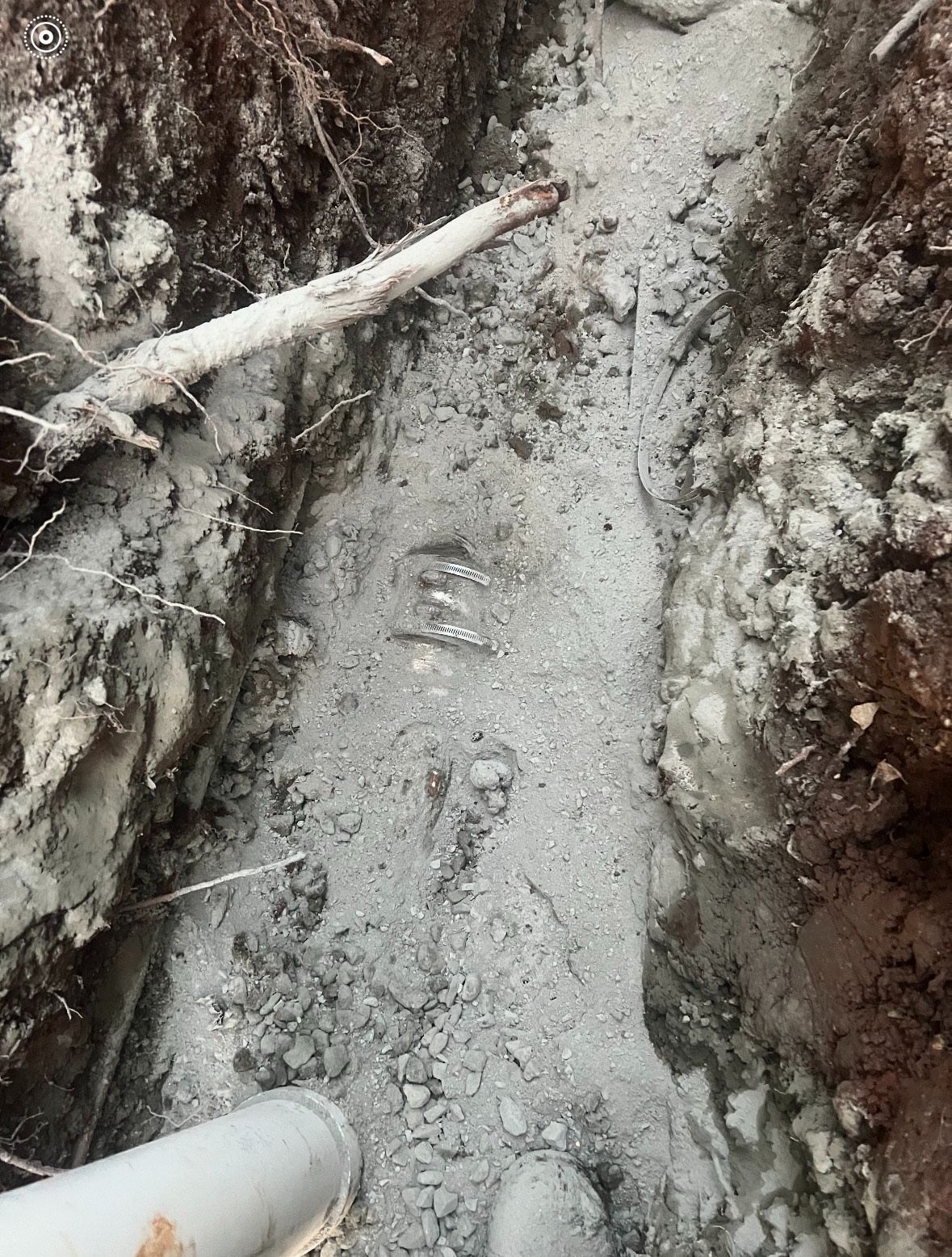 A narrow trench filled with light-colored material, likely cement or gravel, with a PVC pipe visible at the bottom left.