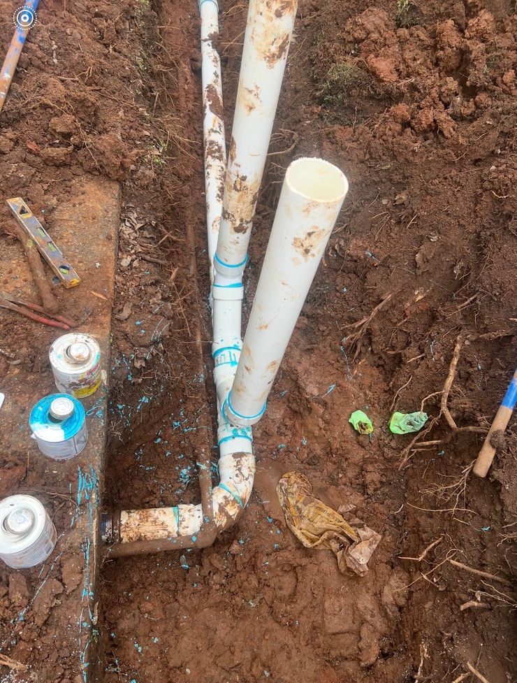 White PVC pipes joined in a dirt trench, likely for irrigation.