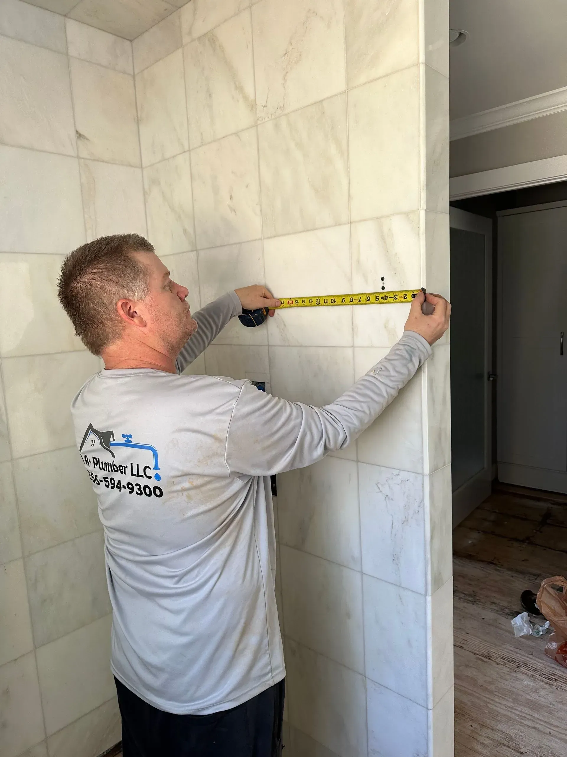 Man measuring a tiled shower wall with a yellow tape measure.