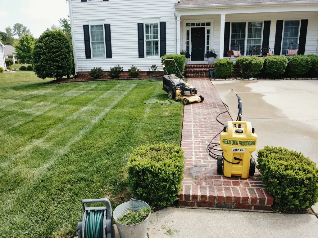 Landscaped front yard with striped lawn, brick walkway, and yellow lawn equipment by a white house.
