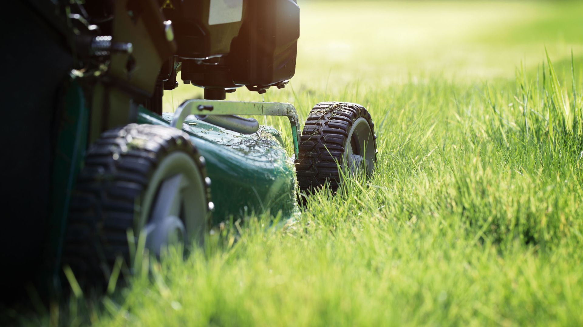 Lawn care worker mowing a green front yard with a push mower, facing a white house and driveway.