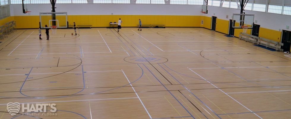 A basketball court with a wooden floor and yellow walls, on a Hart's Athletic installed floor.