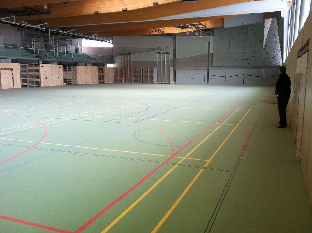 A man stands in an empty gym with a green floor, on a Hart's Athletic installed floor.
