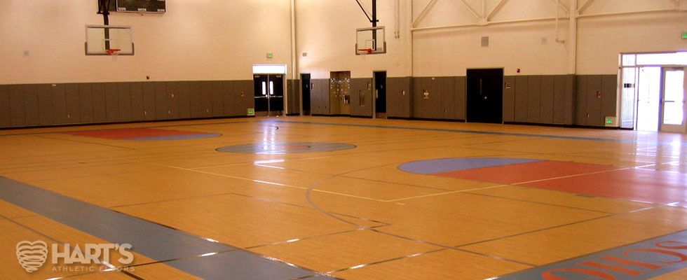 An empty gym with a basketball court and a basketball hoop, on a Hart's Athletic installed floor.