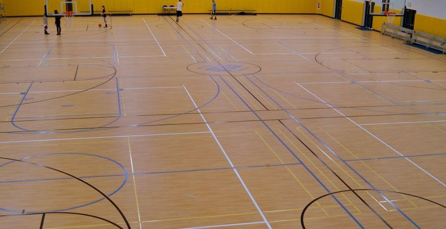 A basketball court with a wooden floor and a yellow wall, on a Hart's Athletic installed floor.