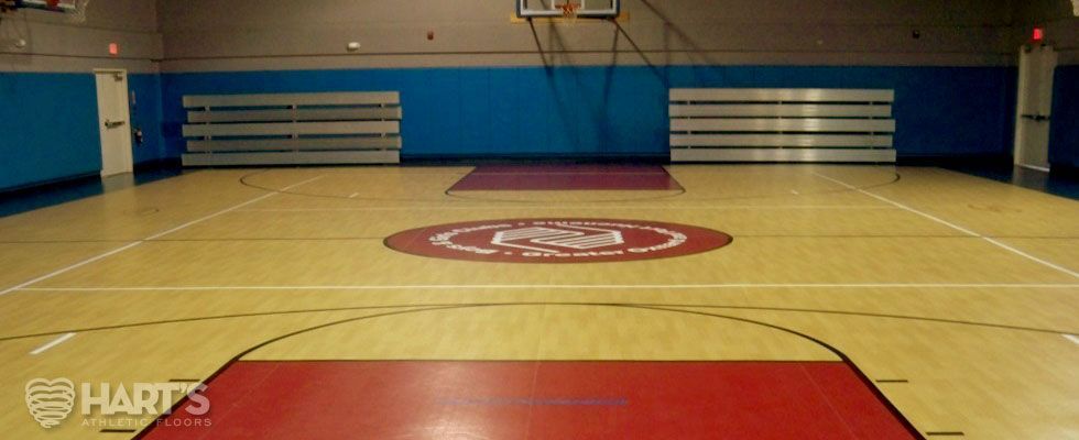 A basketball court with a logo on the floor and a basketball hoop, on a Hart's Athletic installed floor.