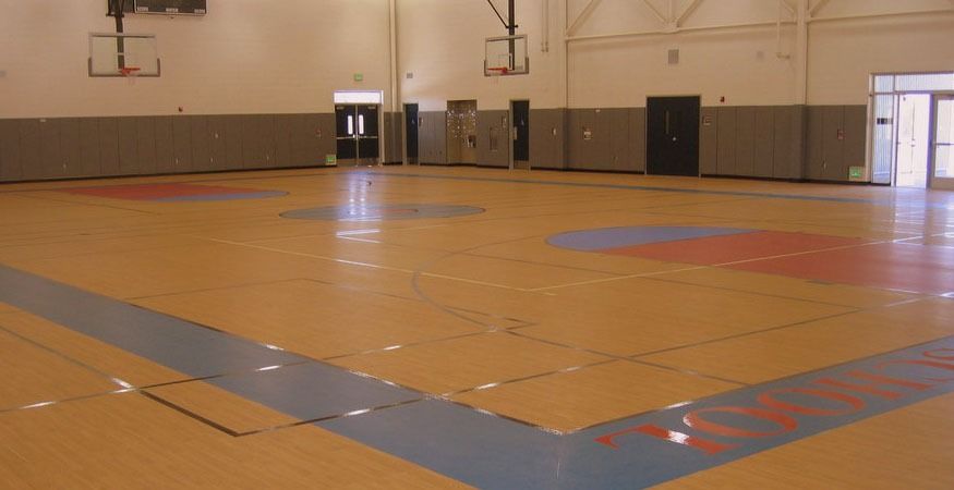 An empty gym with a basketball court and a basketball hoop, on a Hart's Athletic installed floor.
