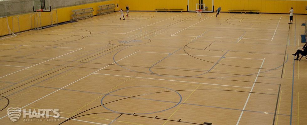 A group of people are playing a game of basketball in a gym, on a Hart's Athletic installed floor.