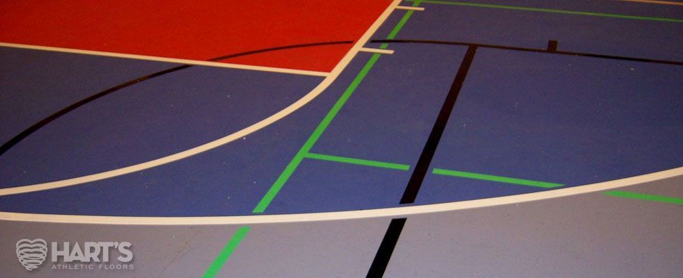 A basketball court with red , blue , and green lines, on a Hart's Athletic installed floor.