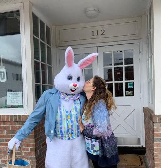A woman kisses a bunny mascot in front of a building with the number 112 on it