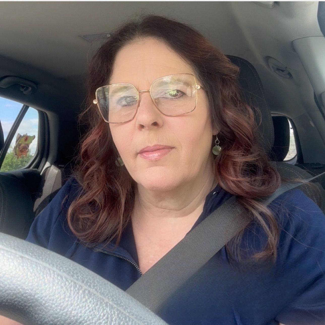 A woman wearing glasses is driving a car with a quote that says we do n't always grow through what we go through