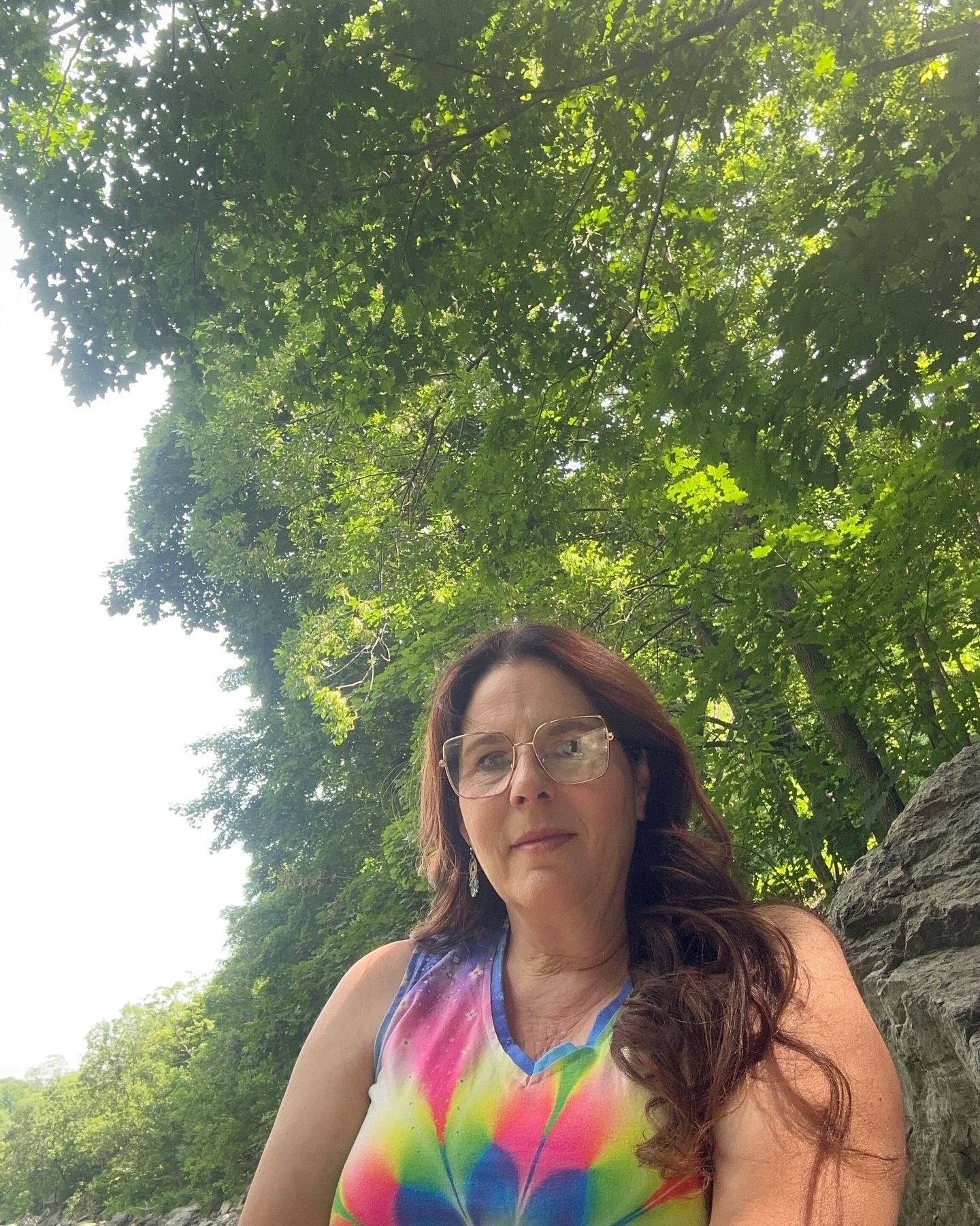 A woman wearing glasses is standing in front of a tree.