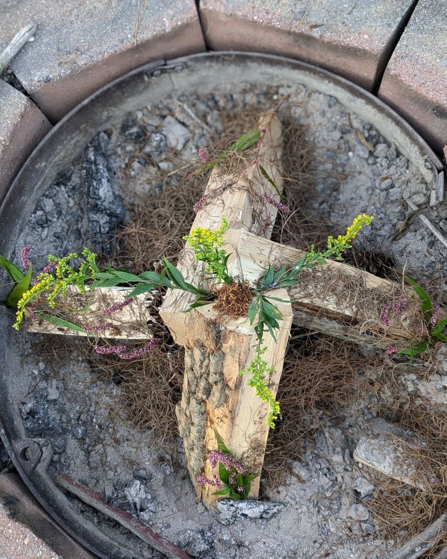 A fire pit with a cross made out of logs and flowers.
