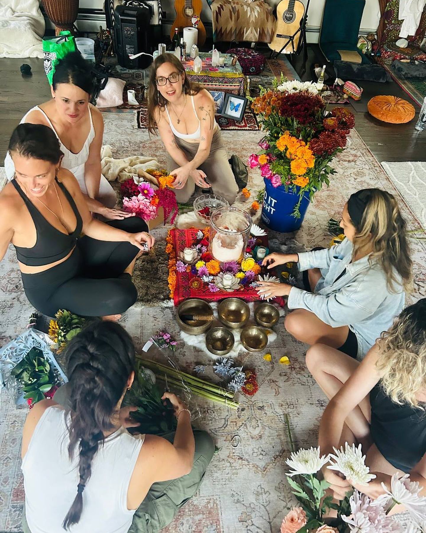 A group of women are sitting around a table with flowers and bowls.