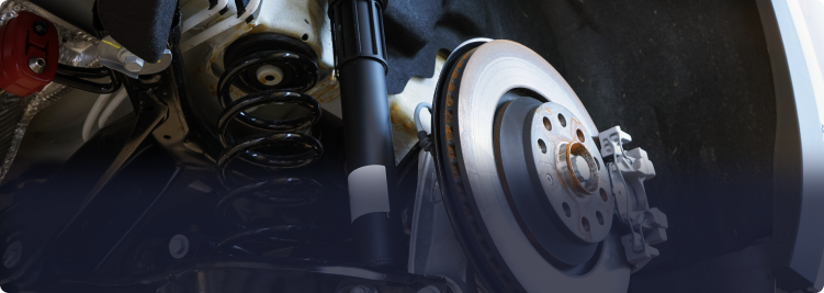Close-up of a car's rear wheel assembly, showing the brake disc, caliper, shock absorber, and suspension spring | Depot Auto Repair