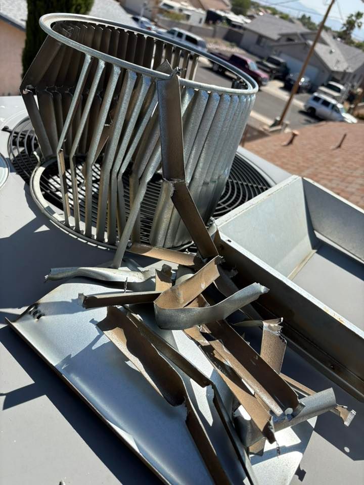 Damaged rooftop air conditioner: bent metal fan cage and scattered debris on a grey unit in a residential setting.