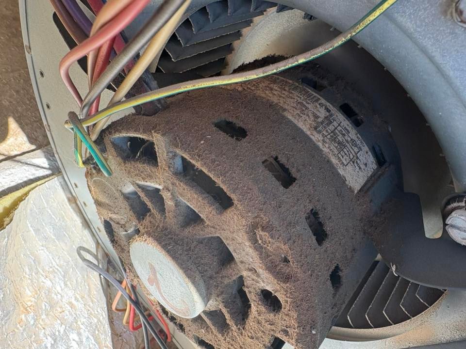 Close-up of a dirty HVAC motor, covered in dust and debris. Various colored wires are connected to it.
