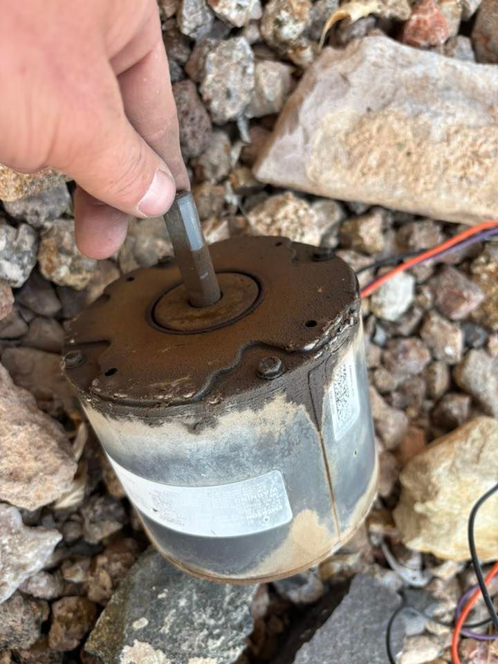 A hand holding a hex key inserted into the shaft of a dirty electric motor, lying on a rocky surface.