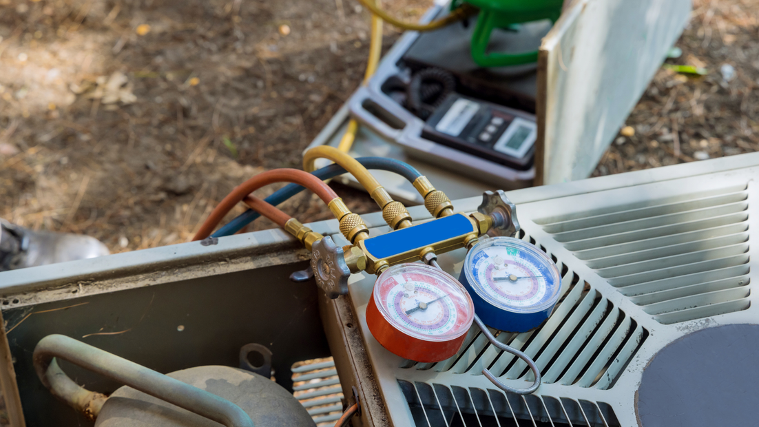 HVAC technician servicing an air conditioner with gauges connected to refrigerant lines outdoors.