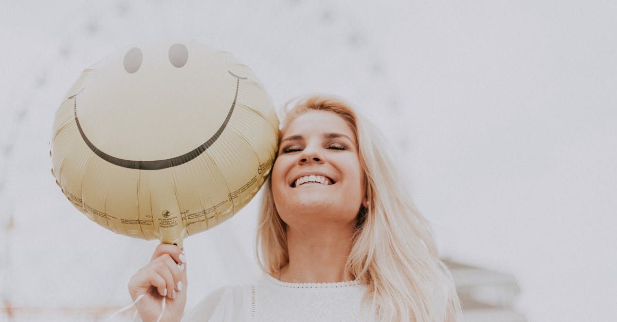 Blonde Frau mit einem Lächeln und einem Ballon mit Smiley.