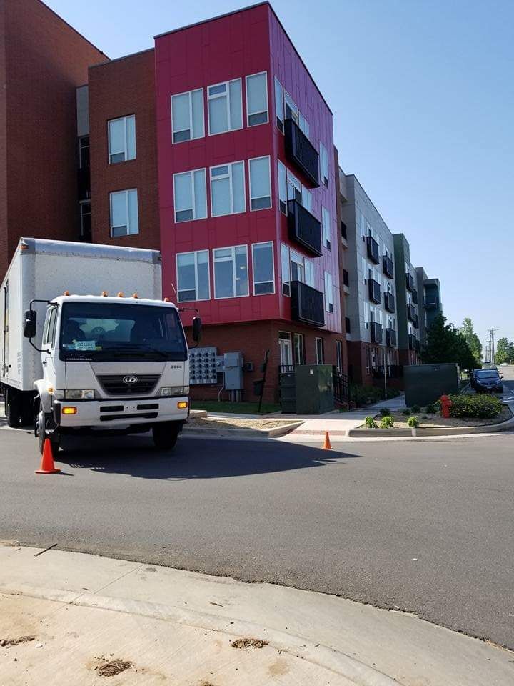 Moving truck parked in front of a multi-story building, painted red, brown, grey, and green.