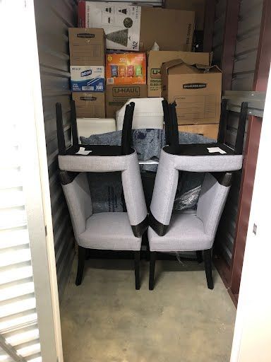 Two gray armchairs stored in a storage unit with boxes behind them.