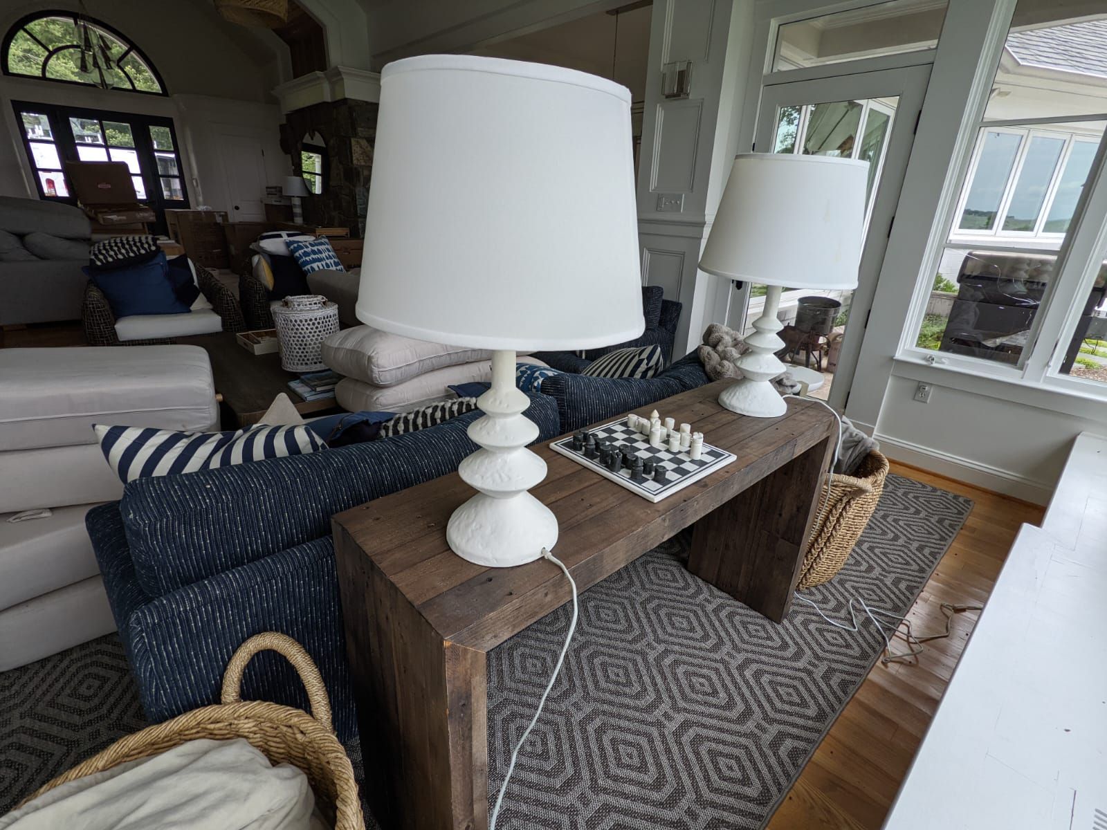 Two white lamps on a wooden console table, chess set, and blue and white sofa in a bright living room.