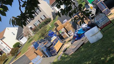 Boxes and furniture piled on a lawn during a move in front of a house. Moving company sign in the grass.