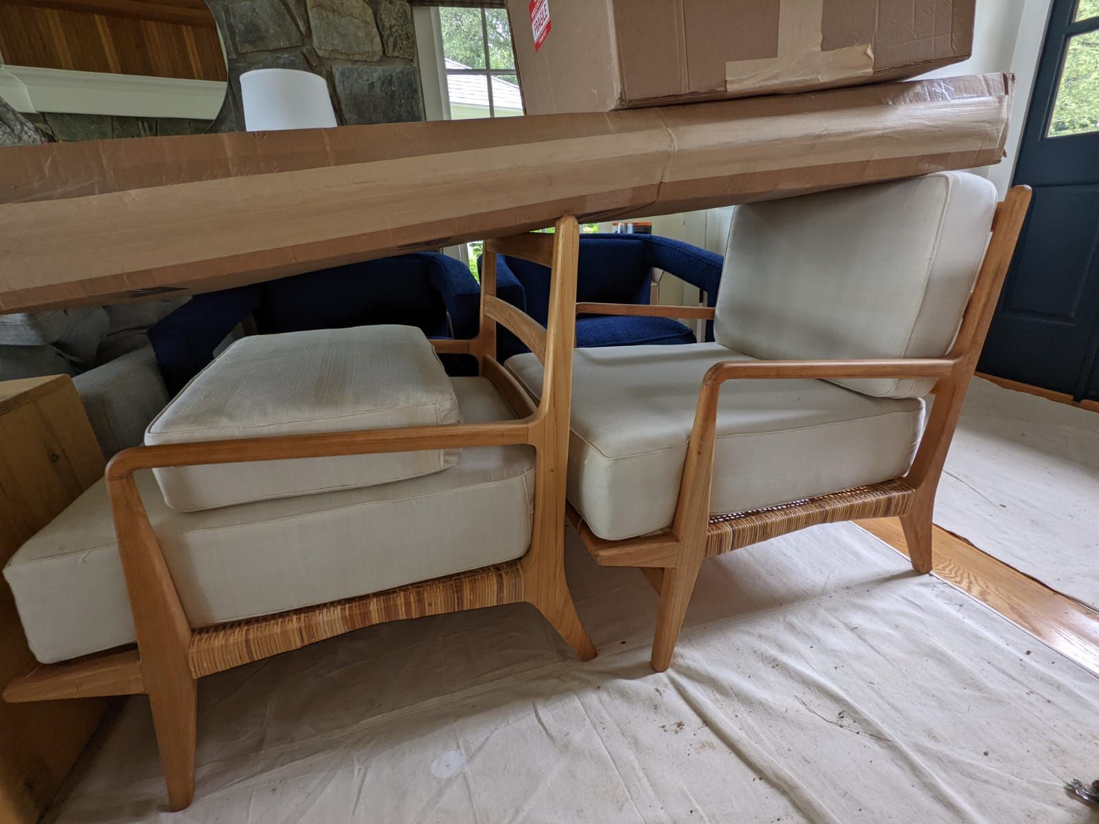 Two wooden chairs with light cushions; cardboard boxes overhead; set on a white sheet indoors.