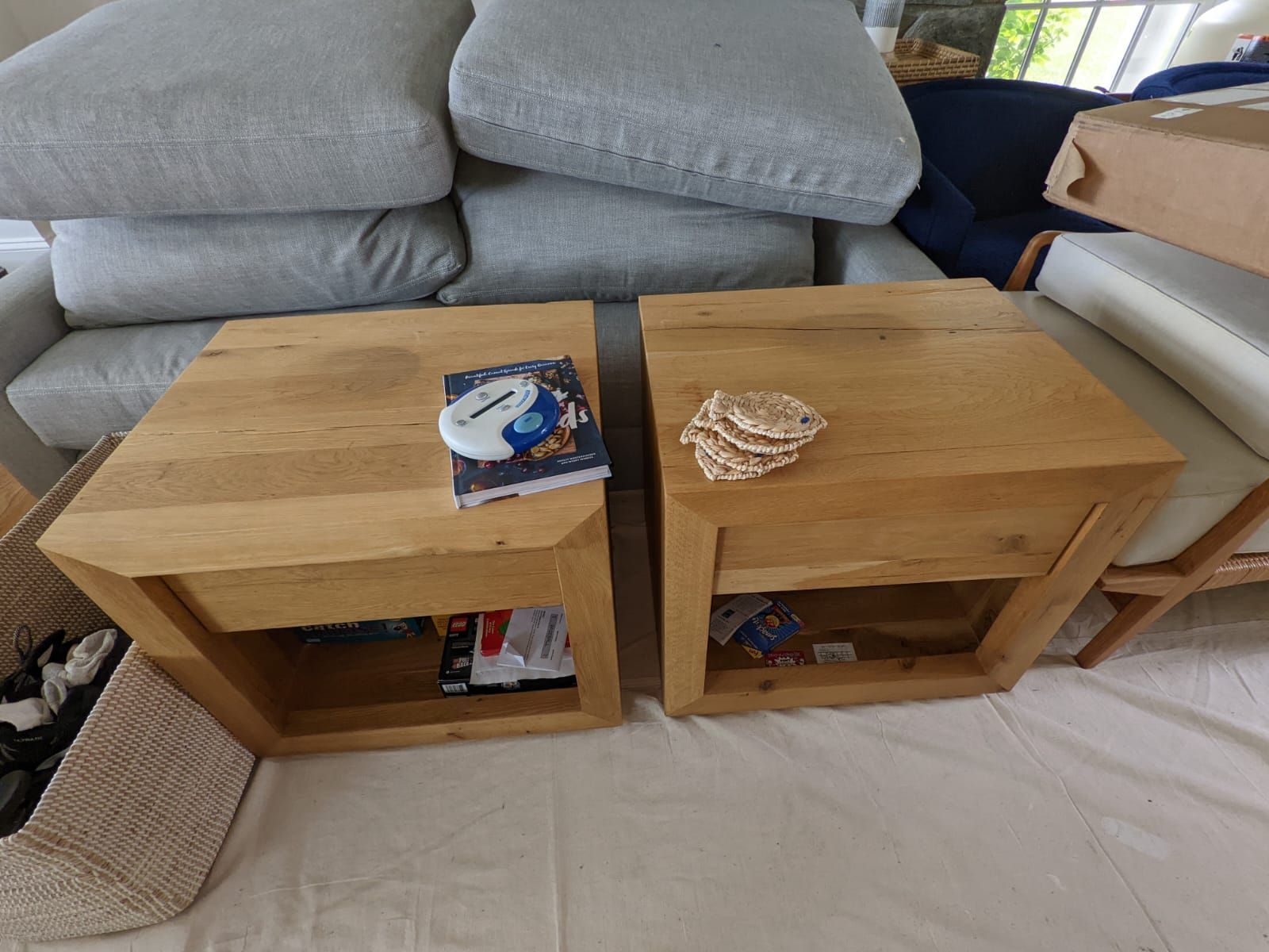Two wooden end tables sit in front of a gray sofa. One has coasters and the other has a book.