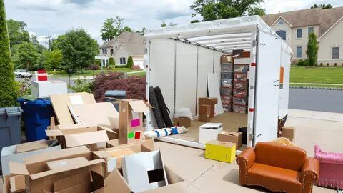 Boxes and furniture scattered around a moving truck in front of a house during a move.