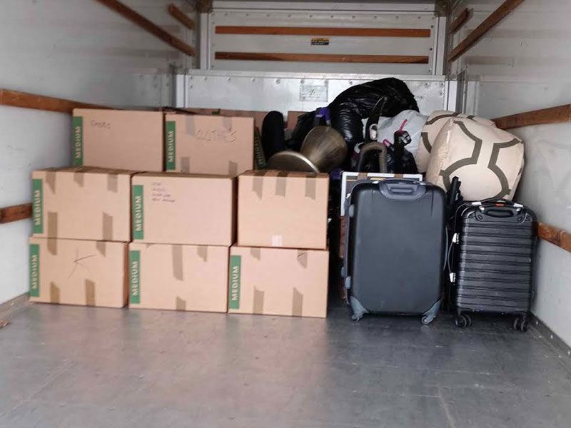 Moving truck interior loaded with boxes, luggage, and various household items.