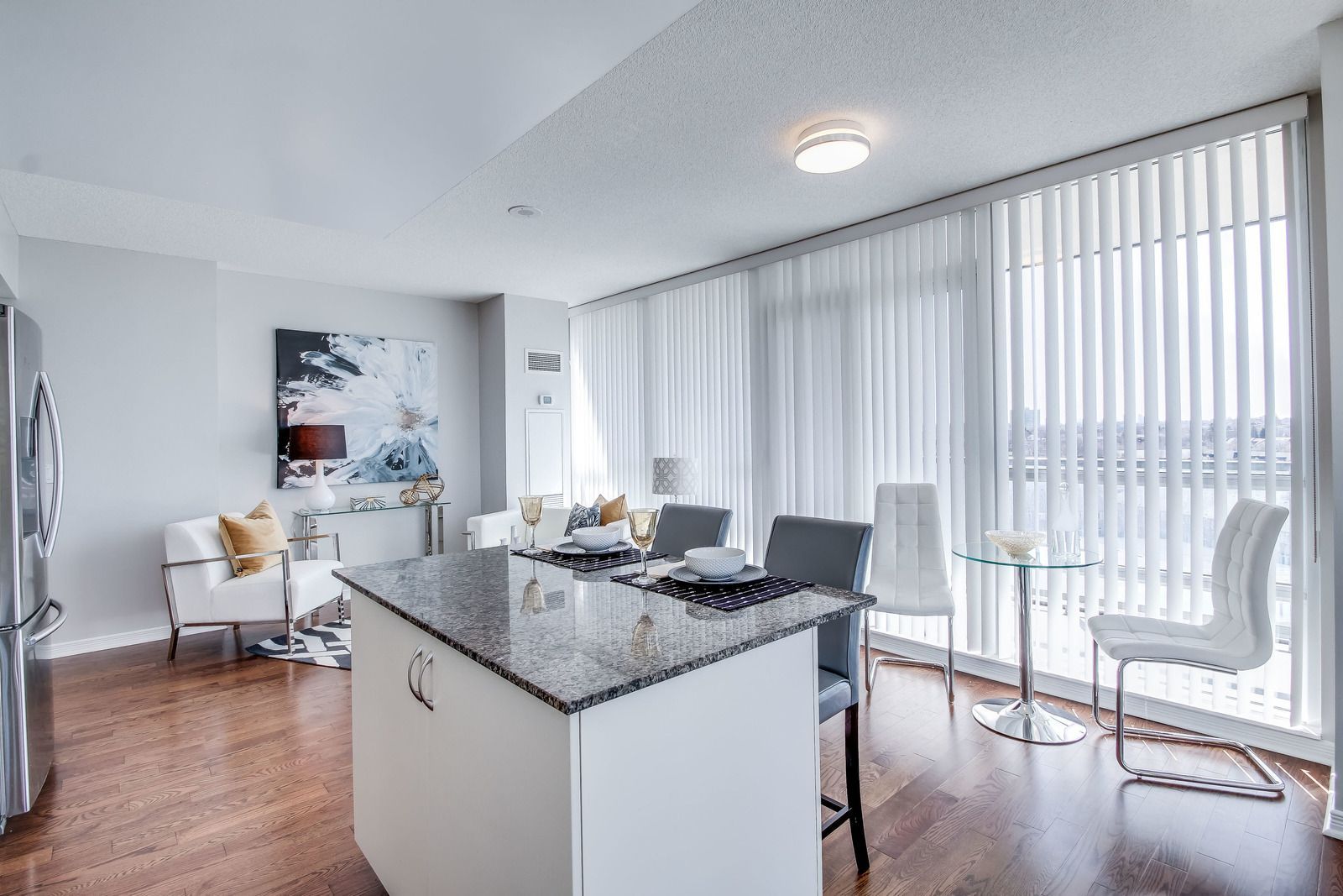 Open-concept condo with a kitchen island, dining area, & living room; white walls, wood floors, and floor-to-ceiling windows.